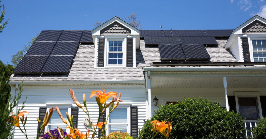 A low-angle view of a home with solar panels on the roof under bright sunlight