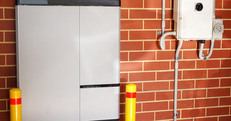 A large lithium-ion solar battery system next to two yellow posts. The system is installed on a brick wall.