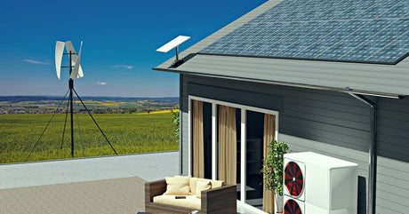 A house situated in an open field and outfitted with solar panels on the roof. There are other homes visible in the distance.