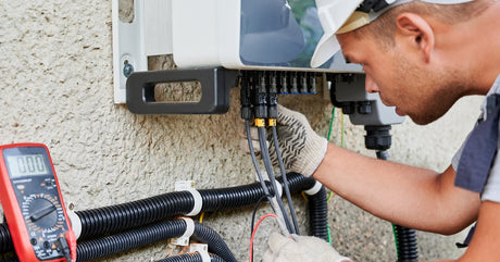 A man in a hard hat and gloves stands in front of an electrical box and carefully installs a solar inverter.