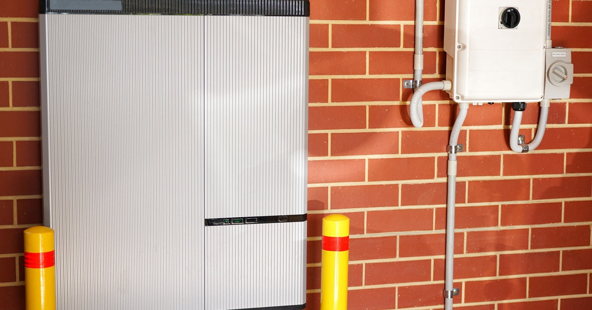 A lithium-ion battery and a solar inverter are installed beside each other inside a brick-walled garage.