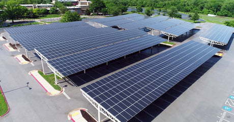 Multiple large solar panels installed in a parking lot in such a way that cars can park in the shade beneath them.