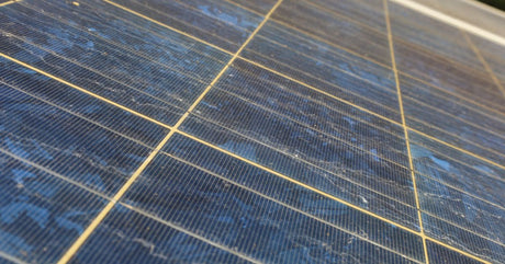 A close-up of a large solar panel installed at an angle. The panels are dirty and dusty, and there are a few cracks.