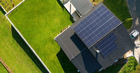 An aerial view of a house with a large green lawn. There are several solar panels installed on the roof.