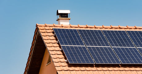 A medium-sized home with an angled roof has several solar panels installed on it. The roof has a small chimney.